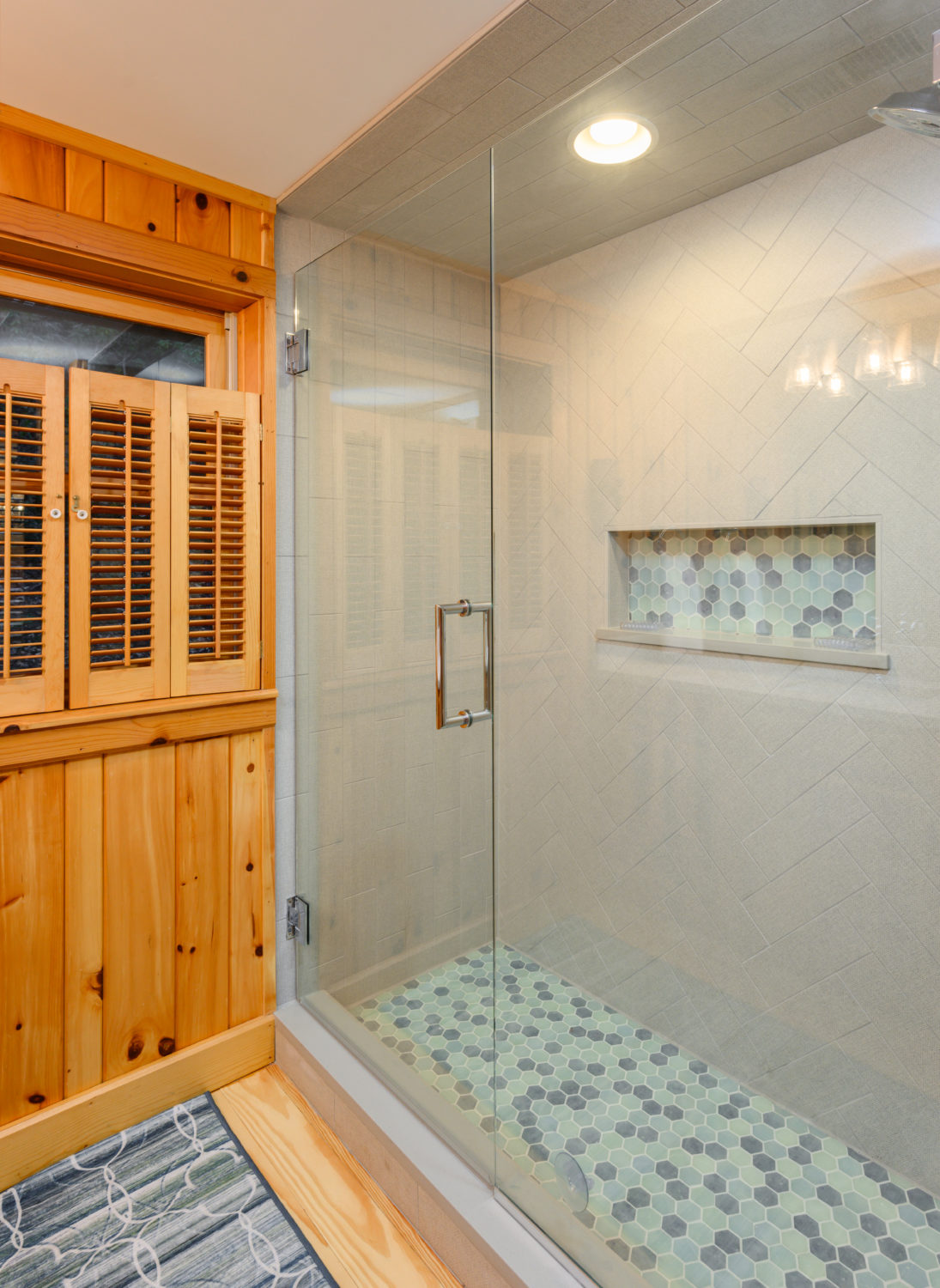 Glass enclosed shower uses a herringbone tile pattern for the wall but a blue mosaic pebble for the floor