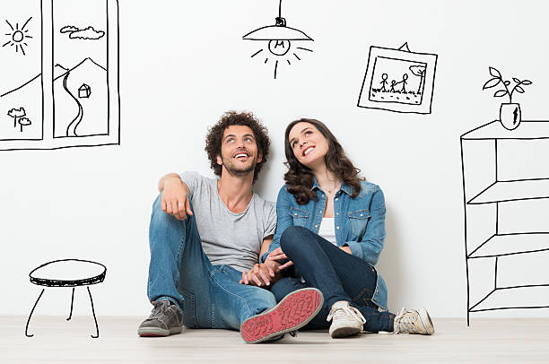 Portrait Of Happy Young Couple Sitting On Floor Looking Up While Dreaming about their remodel